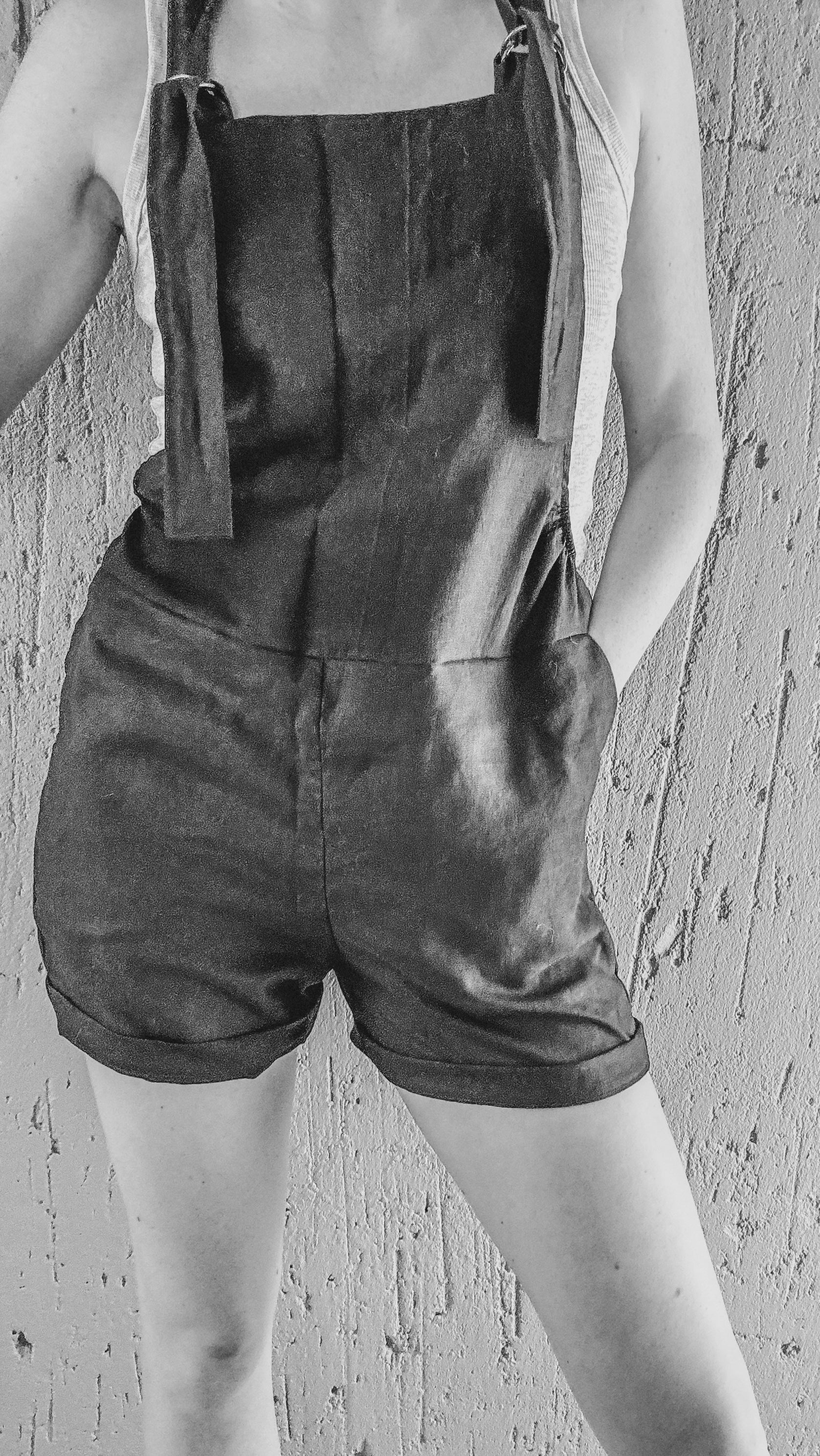 Person wearing a black short overall style romper made from pure black linen with adjustable straps and side pockets.