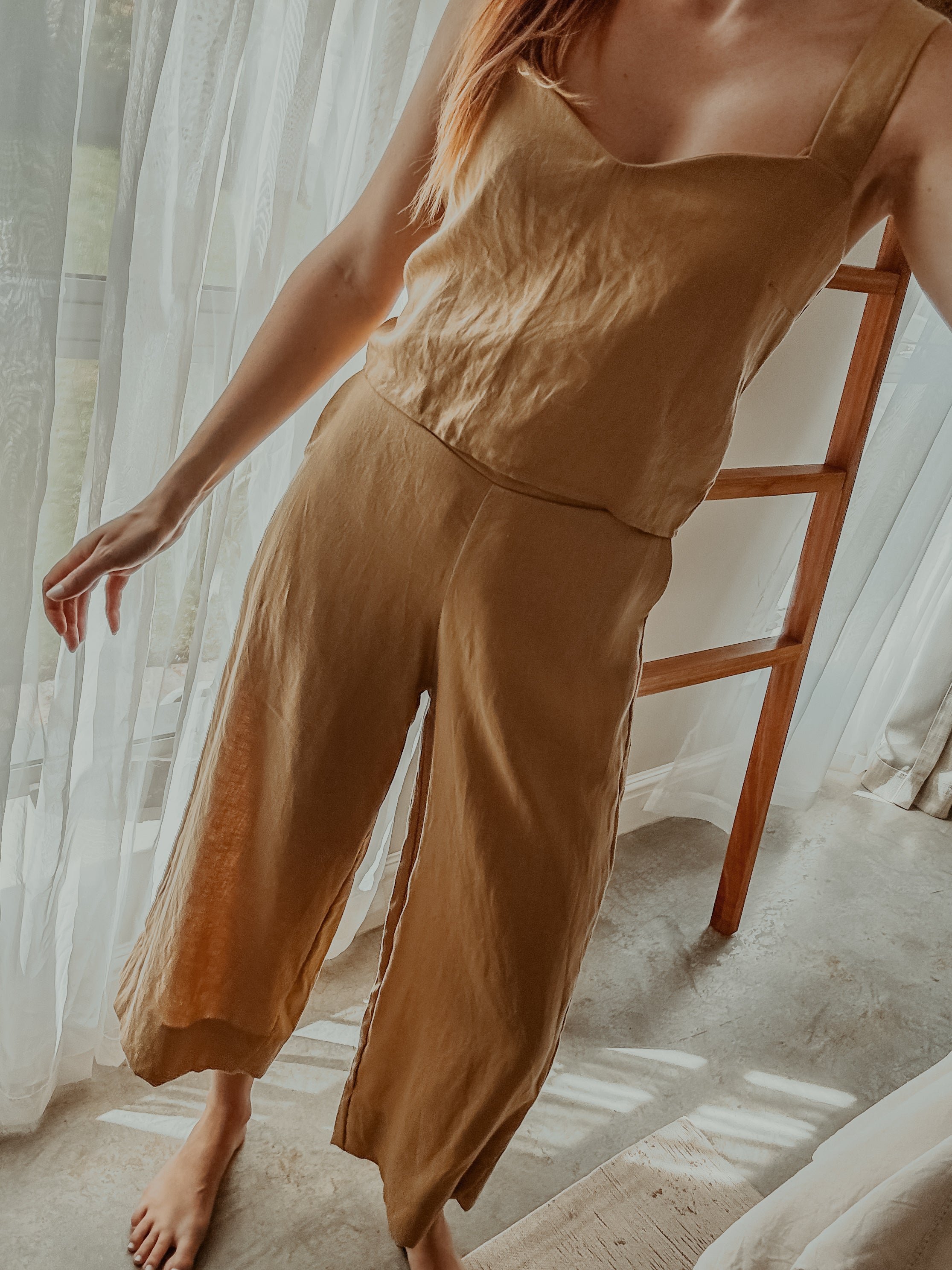 Person wearing a sand colour matching sleeveless top and wide-leg pants with broad hem, standing in a softly lit room.