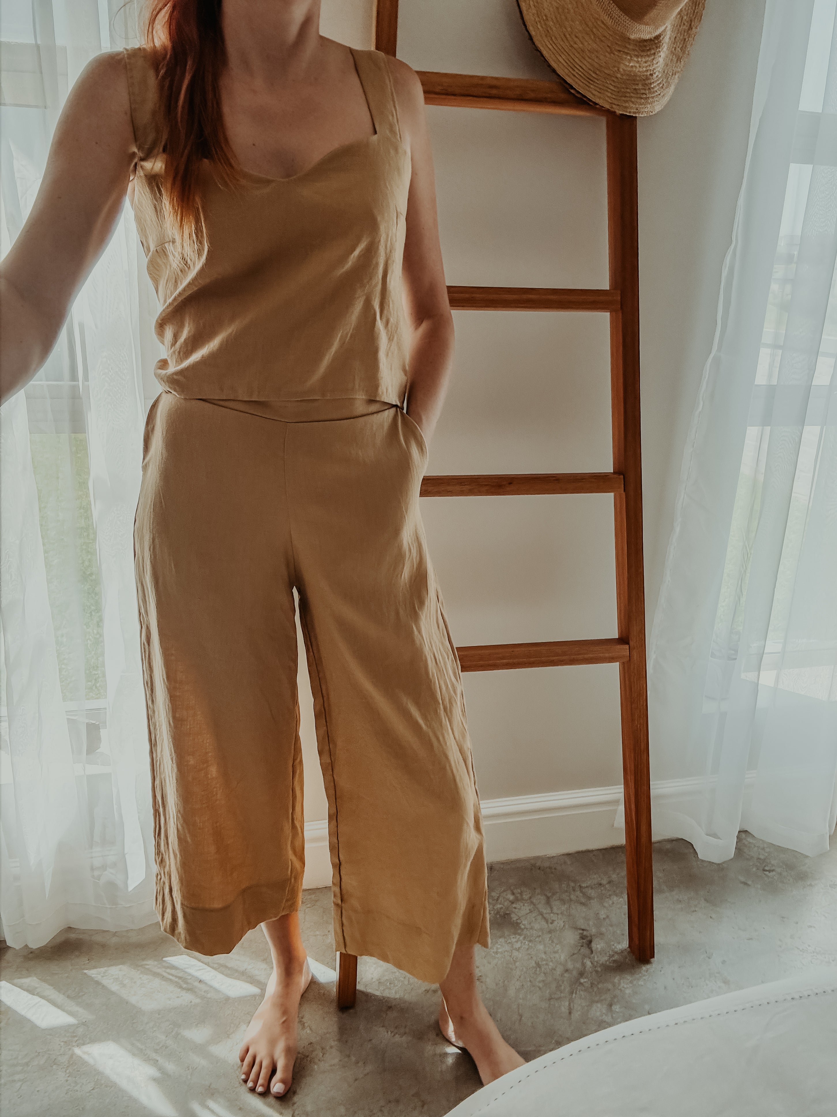 Person wearing a beige sleeveless top and wide-leg pants standing with one hand in side pocket.