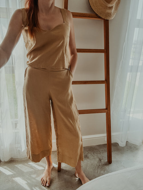 Person wearing a beige sleeveless top and wide-leg pants standing with one hand in side pocket.
