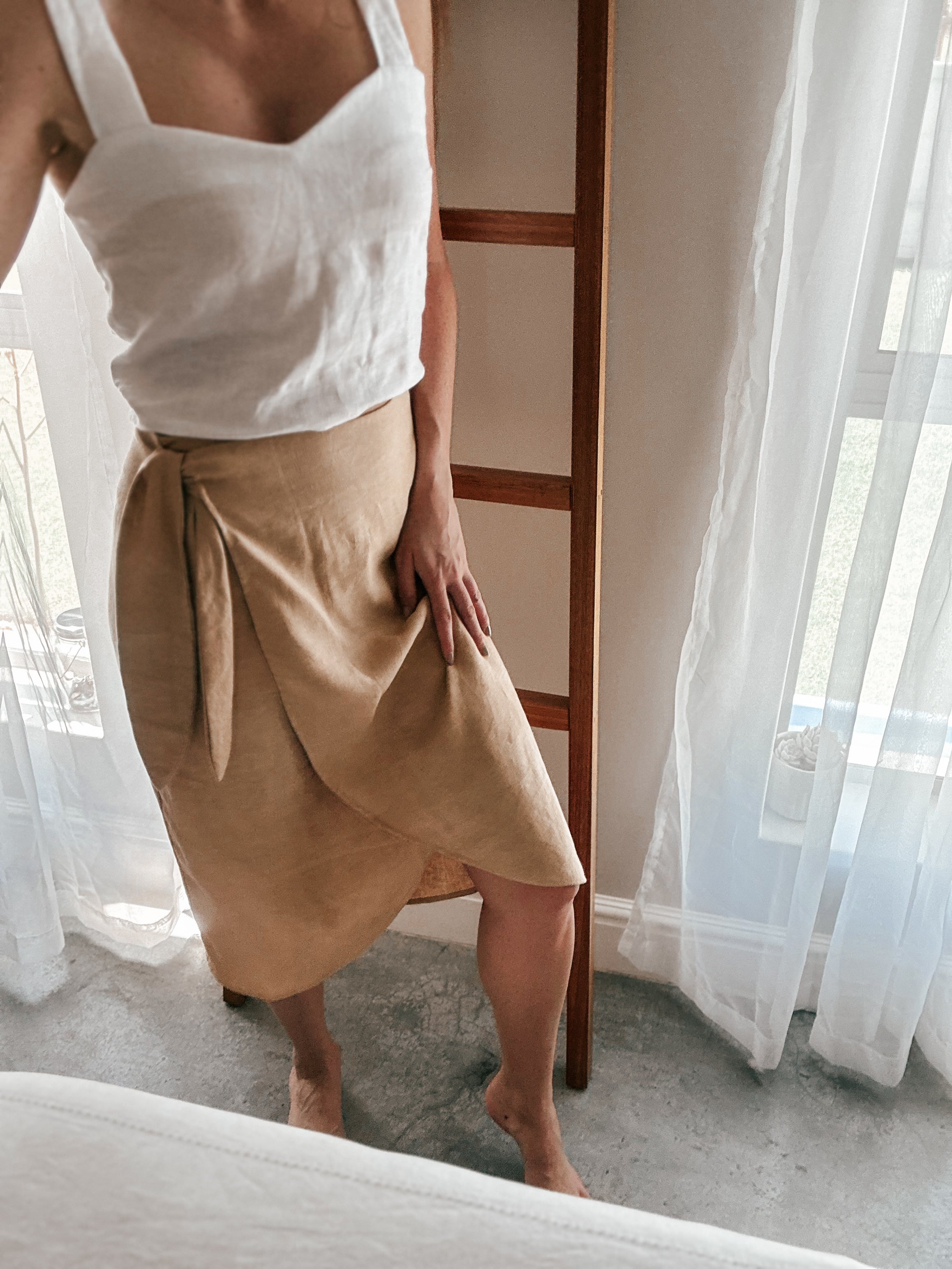 Person wearing beige sand colour wrap skirt in midi length and curve hem.