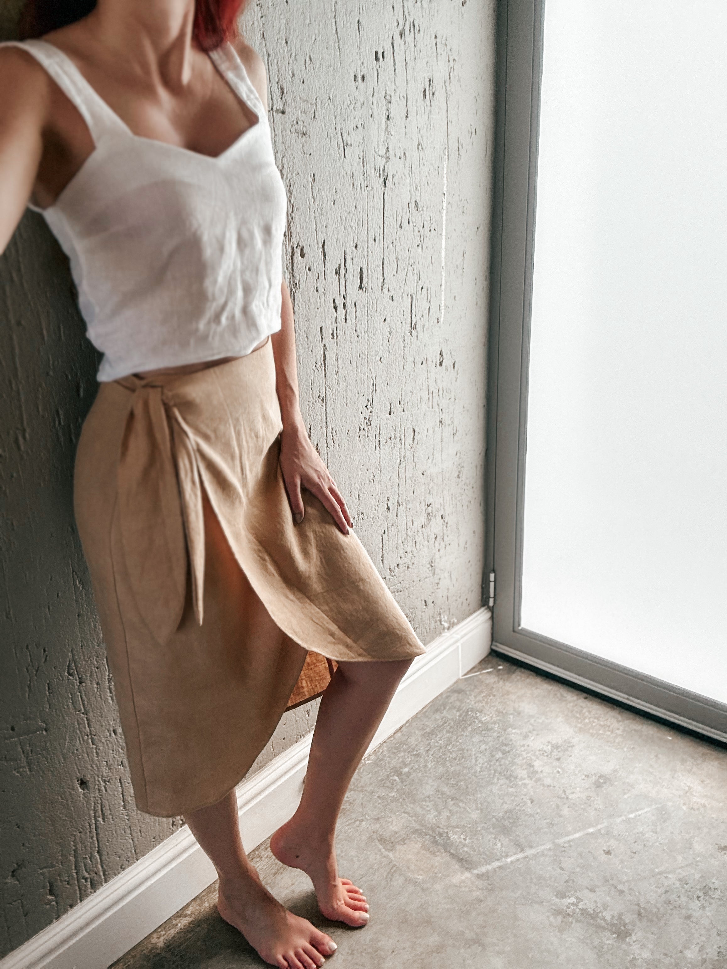 Person wearing a pure linen white tank top and beige skirt with curve front hem and side knot detail.